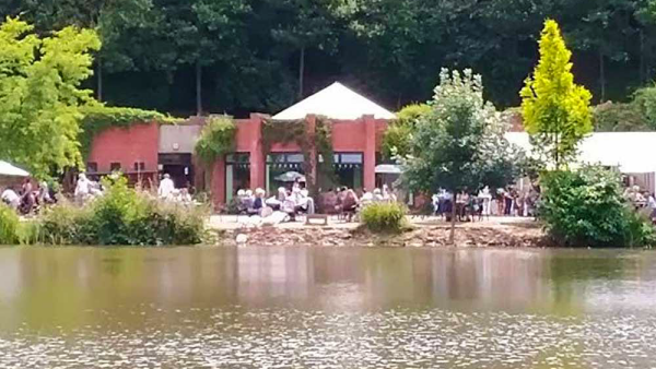 Several visitors enjoying the lakeside cafe outdoor seating area during a sunny day at Bodenham Arboretum