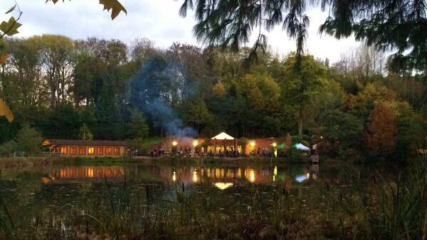 Latenight dining at the lakeside cafe at Bodenham with visitors enjoying the view. The cafe is lit from within, and a barbecue smoke rising in to the sky.
