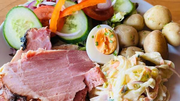 A plate of food with roasted meat, salad greens, potatoes, and a portion of coleslaw. The plate is on a table.
